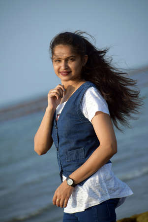 Pretty girl looking at the camera standing in front of the sea. Beautiful woman wearing jeans and...