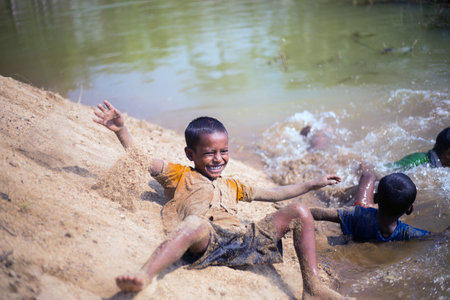 Taherpur, Bangladesh â November 05, 2019: Children toppling from the sands of the riverbank down to the water. Little kids enjoying tumbling with the sands and bathing in a river.のeditorial素材