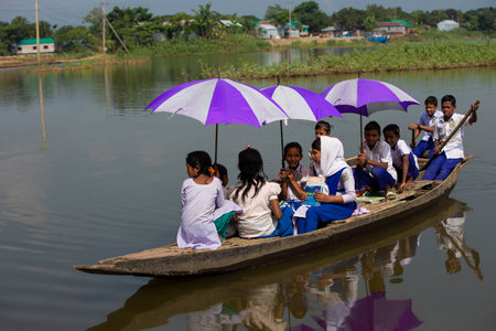 Taherpur, Bangladesh â November 05, 2019: School boys and girls coming back from school by boat. School children boating, and rowing paddle with school dresses and colorful umbrellas going to school.のeditorial素材