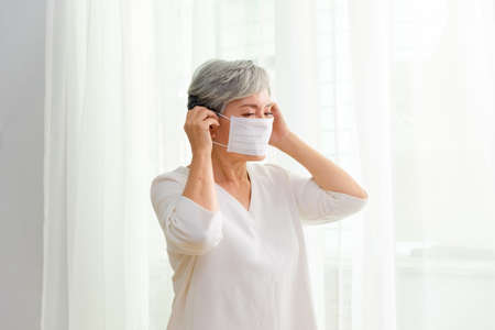 Brave woman with gray hair wearing mask by the windowの写真素材
