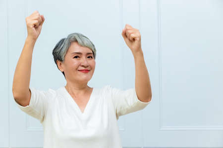 Senior beautiful asian woman wearing casual dress standing and raising fists.