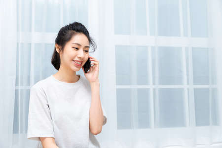 Asian young girl talking on the phone in front of big windowの写真素材