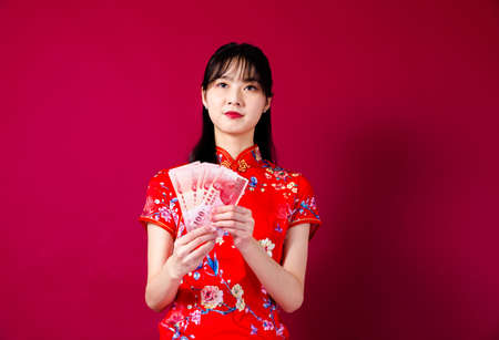 Beautiful Asian girl in traditional cheongsam on red background holding red envelope.