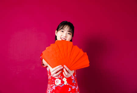 Beautiful Asian girl in traditional cheongsam on red background holding red envelope.の写真素材