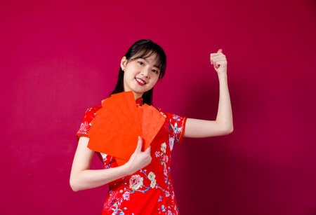 Beautiful Asian girl in traditional cheongsam on red background holding red envelope.の写真素材