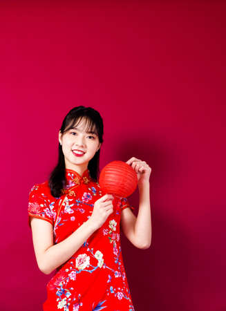 Beautiful Asian girl in traditional cheongsam on red background holding a lantern. Translation- blessing.の写真素材