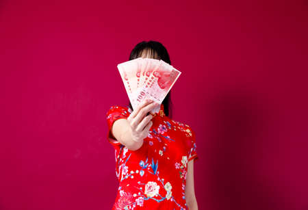 Beautiful Asian girl in traditional cheongsam on red background holding red envelope.の写真素材