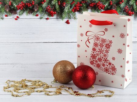 Christmas composition of gold and red Christmas balls, gift bag and 
gold stars on a light wooden surface and background with fir border. 
Christmas, winter, New Year concept. Front view. With copy spaceの写真素材