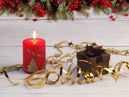 Christmas composition of the burning red Christmas candle, gift 
box and gold stars on a light wooden surface and background with fir 
borderの写真素材