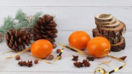 Christmas composition of pine cones, tangerines, anise, glittered 
hazelnuts, saw cut wood pieces and pine tree branch on light wooden 
surface and backgroundの写真素材