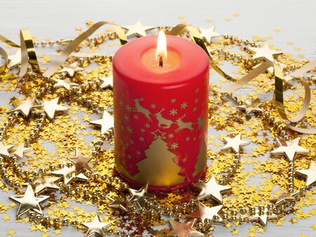 Christmas composition of the burning red Christmas  candle, gold stars 
and garland on a light wooden surfaceの写真素材