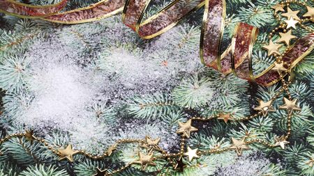 Christmas background with ribbon and gold star garland on snow covered green pine surfaceの写真素材