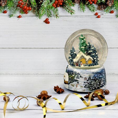 Christmas composition of snow globe, anise, and glittered hazelnuts on light wooden surface and background with fir border. With copy spaceの写真素材