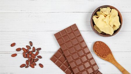 Bars of milk chocolate, cocoa butter, cocoa powder and cocoa beans on light wooden background. Top...