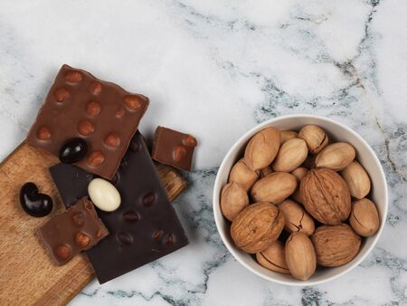 Broken chocolate bars, raw inshell and chocolate covered nuts on gray marble background. Top view with copy spaceの写真素材