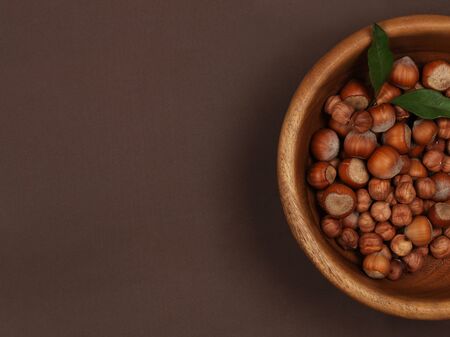 Raw hazelnuts in a wooden bowl on brown suede background. Top view with copy space