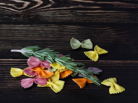 Dried colorful Italian pasta farfalle or bows with rosemary on dark wooden background. With copy...