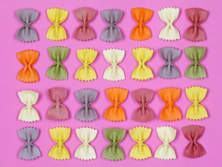 Dried colorful Italian pasta farfalle or bows on bright pink background