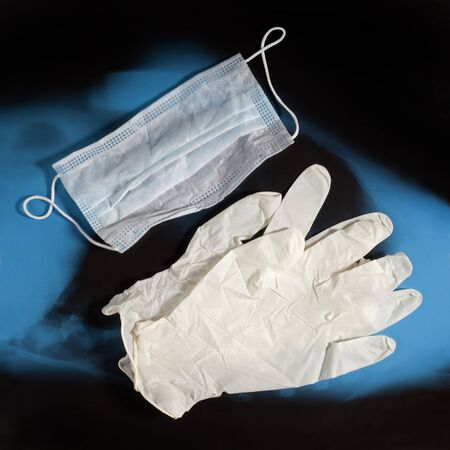 Pair of latex medical gloves and ear-loop mask on blue black X-ray image background. Protection...
