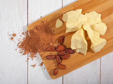 Pieces of natural cocoa butter, cocoa powder and cocoa beans on wooden cutting board. Top view. Flat layの写真素材