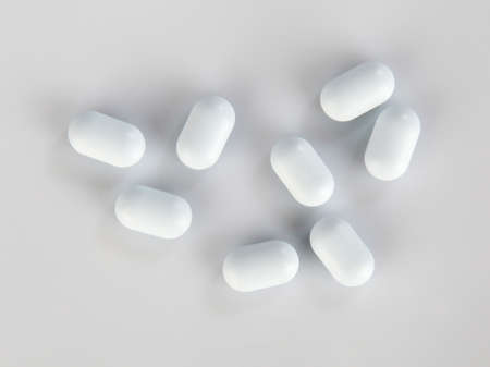 Top view on white big oval pills scattered on gray background. Close-up shot