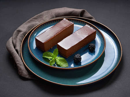 Two cakes covered with chocolate frosting with blackberries and mint on blue plates