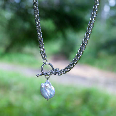 Baroque pearl pendant with silver chain on green nature backgroundの写真素材