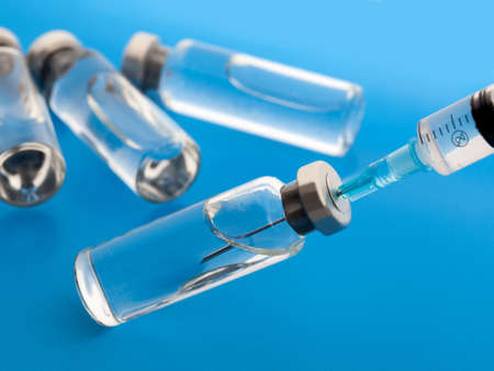 Close-up medical syringe and vials with medicine for injection. On blue background