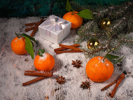 Christmas composition of tangerines, anise, cinnamon, gift box, balls and fir tree branch on wooden snow covered surfaceの写真素材