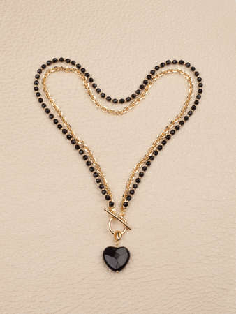 Female heart shaped pendant with golden chain necklace on beige leather background. top viewの写真素材