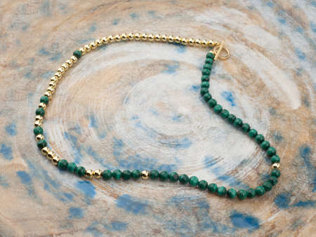 Golden necklace with green gemstones on spotted background. close-up shotの写真素材