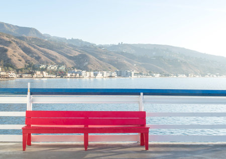 solitary red wooden bench against a blue and white railing overlooking the Pacific ocean in Malibu, Californiaの写真素材