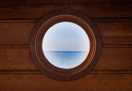 view of the Pacific ocean through a round portole window in a weathered wooden wallの写真素材
