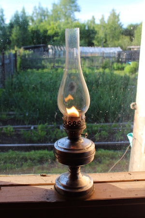 An old-fashioned kerosene lamp stands on a wooden window-sill.の写真素材