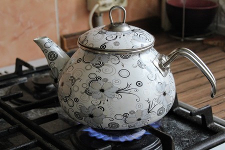 A beautifully painted kettle stands on a gas stove.