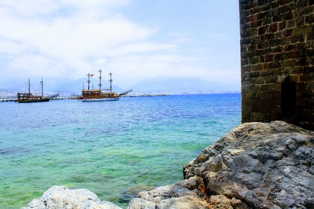 View from the rocky shore to the pleasure boats sailing at anchor in the city harbor (Alanya, Turkey).の写真素材