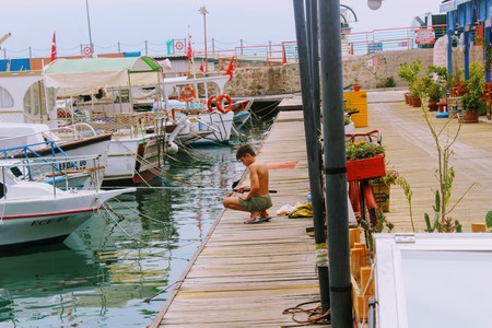 The boy is fishing on the fishing pole from the pier in the city harbor (Antalya, Turkey).のeditorial素材