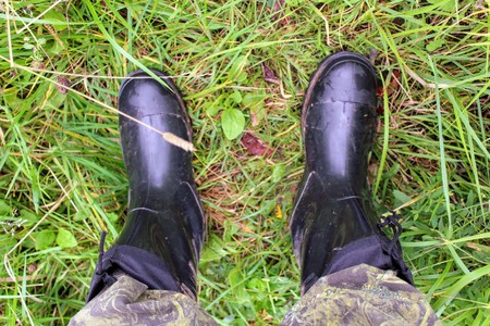 Male feet in black rubber boots lie on the grass.の写真素材