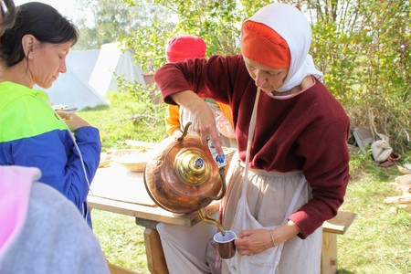September, 16 2017, Tula, Russia - The International Military and Historical Festival "Kulikovo Field": a woman in traditional clothes pours sbiten from a copper kettle.のeditorial素材