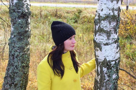 Autumn time: beautiful girl in a yellow coat posing against an autumnal birch forest.の写真素材