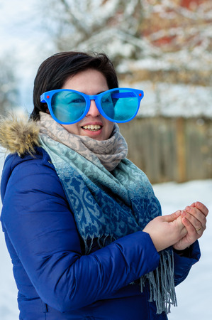 European brunette girl in big clown glasses with scarf, smiling, standing alone rubbing his hands in cold winterの写真素材