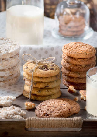 Homemade oatmeal and chocolate chip cookies in rustic wooden tray, glass of milk, bottle, cozy early breakfast conceptの写真素材