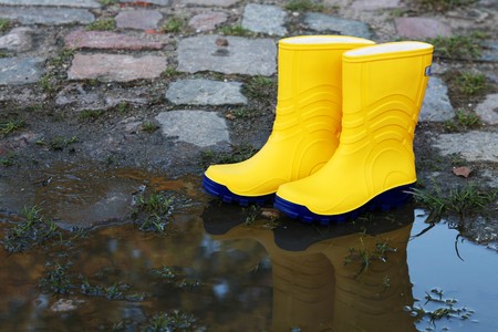 Pair of yellow rubber boots beside a puddleの写真素材