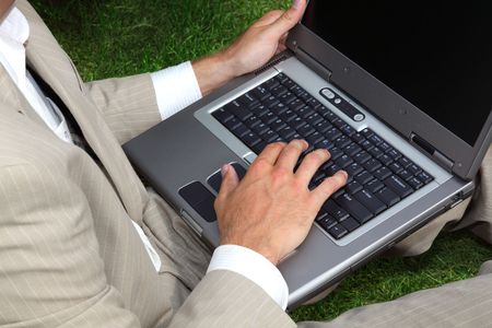 Businessman sitting in the grass using a laptopの写真素材