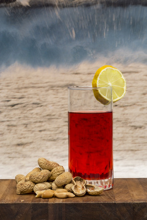 glass of vermouth with  peanuts on a wood table over waves crashingの写真素材