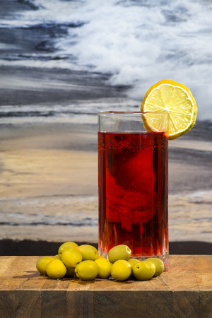 glass of vermouth with olives on a wood table over a sunset on the beachの写真素材