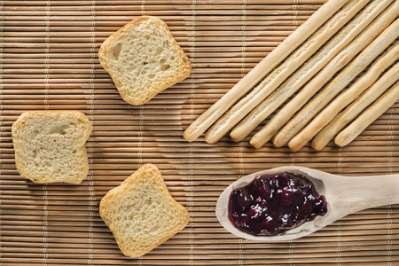 breadsticks, toasts and a spoon of blueberry jam on a wicker matの写真素材