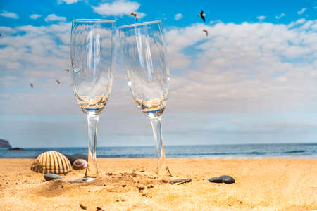 two empty cocktail glasses on the beach with seagulls flying over a blue skyの写真素材