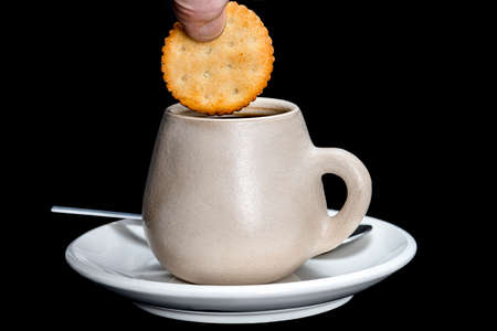 dipping a lemon cookie in a rustic cup with coffee on a black background
