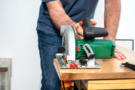 Man with electric circular saw cutting wooden board on white backgroundの写真素材